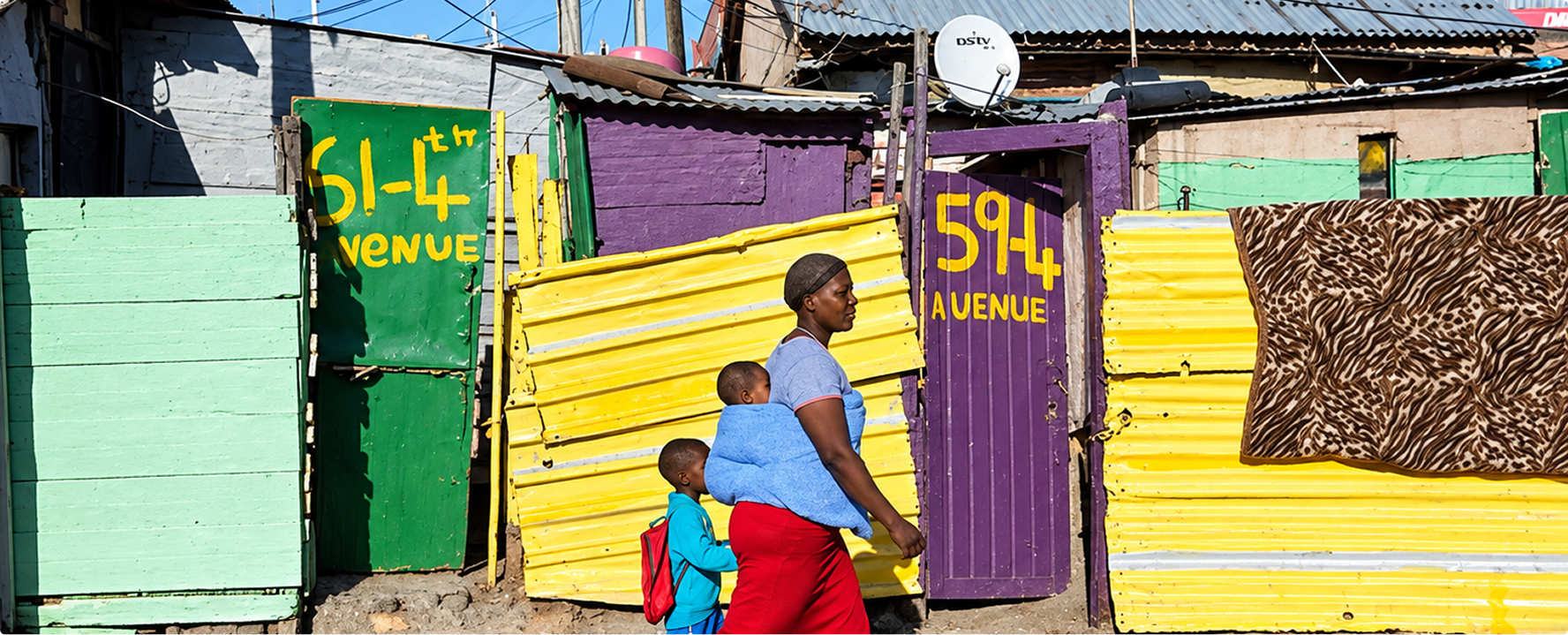 A woman carrying a child walks past painted metal homes marked with street addresses